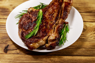 Roasted beef rib eye steak on bone with rosemary in white plate on wooden table