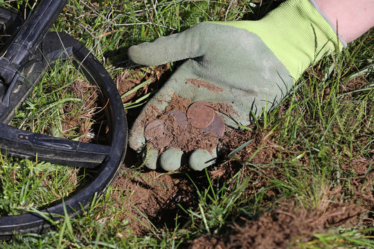 Man holding old coins found in a field with metal detector 