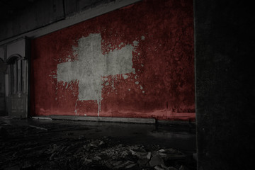 painted flag of switzerland on the dirty old wall in an abandoned ruined house.