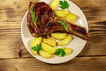 Roasted beef rib eye steak on bone with baked potatoes and herbs on wooden table