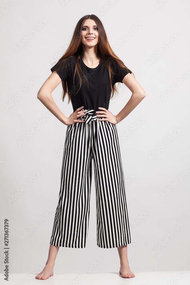 Wall mural Photo of a beautiful slim woman in full growth, dressed in a black blouse and striped pants