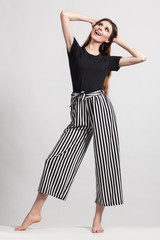 Photo of a beautiful slim woman in full growth, dressed in a black blouse and striped pants