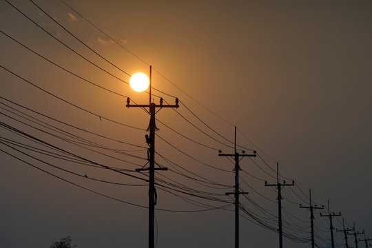 Power line silhouette and it's post with sun is setting in an evening