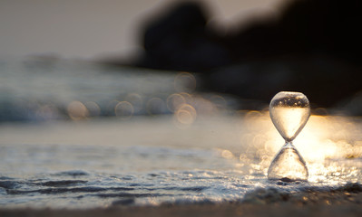An hourglass on a sea beach with gold bubble blur background in an evening
