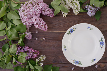 Plate and decor of flowers on the background of vintage wooden planks.Vintage background with lilac flowers and place under the text. View from above. Flat lay. Cutlery.