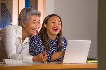 natural lifestyle portrait of two business partners or work colleagues women collaborating and coworking happy and cheerful at office laptop computer desk