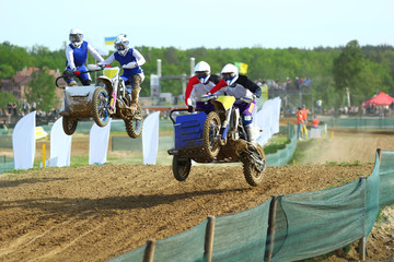 Sidecar motocross athletes overtaking in the air jump on the dirt track 