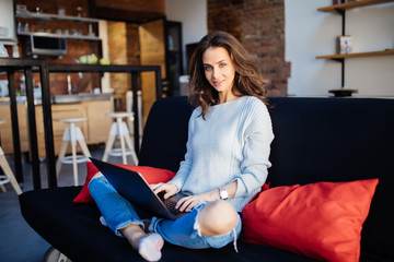 Happy pretty young woman using laptop sitting on cosy sofa