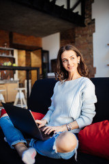 Happy pretty young woman using laptop sitting on cosy sofa