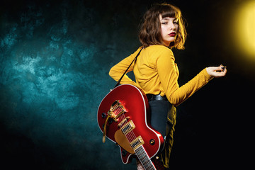 Portrait of beautiful young hipster woman with curly hair with red guitar in neon lights. Rock...
