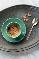 A cup of black coffee, shot from above on a tray with caramelized sugar and a spoon