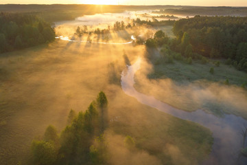 Sunrise over foggy river. Aerial view of river nature in sunlight. Bright sunny morning landscape view from above. Sunrays through mist on meadow