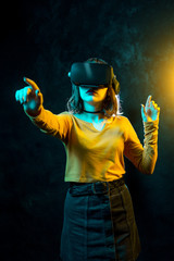 Young hipster woman with curly hair wearing virtual reality goggles and touch another world in studio neon lights. Smartphone using with VR headset.