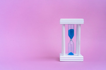 Elegant hourglass with running blue sand on pink background with copy space