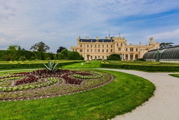 Lednice, Czech Republic - May 28 2019: Famous Lednice castle in South Moravia with yellow facade. Garden with green lawn, flowers and sand footpath. Sunny spring day, blue sky, white clouds.