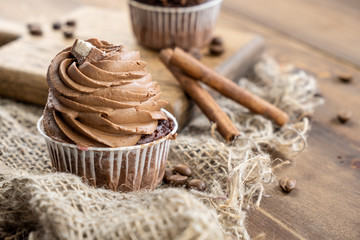 brown cupcakes with cocoa cream, cinnamon and coffee on wooden background