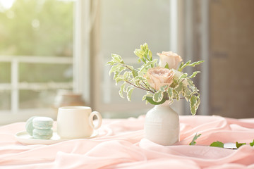 French blue macaroon plate and coffee cup standing on a wooden table with a pink tablecloth white vase with flowers roses and greens.