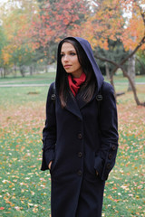 The girl in the black coat looks away from the camera on background of autumn trees.