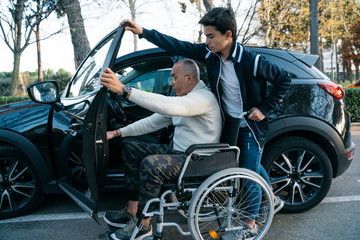 Boy helping his grandpa handicapped to get on the car