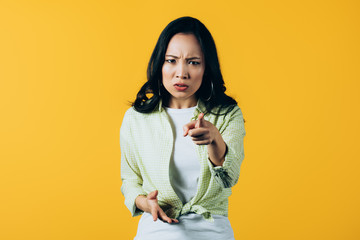 emotional angry asian girl pointing at you isolated on yellow