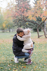 Child hugging and kissing their dad. Father smiles when his daughter ran up to him on the background of autumn park.