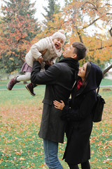 Family on a walk in the park during the first snow. Happy father and mother playing with daughter, throws the girl up in the sky. The emotion of happiness, fun, love.