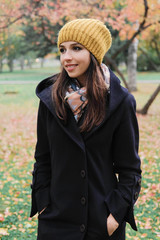 The girl in the black coat looks away from the camera on background of autumn trees.