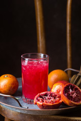 Glass of blood orange juice with ice and orange fruits on dark background