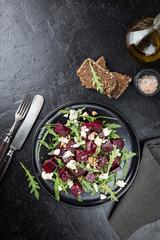 beetroot salad with blue cheese, arugula and walnut in a black plate on stone background, top view