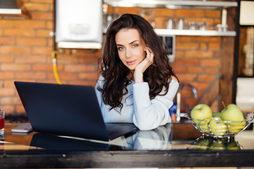 Charming young woman with a laptop in the kitchen