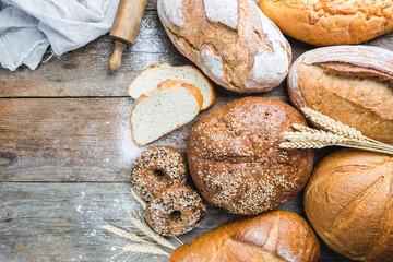 Assortment of fresh baked bread and buns on wooden table background, top view