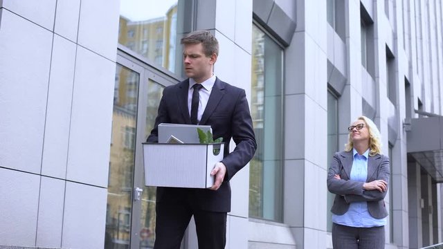 Gloating mature woman looking at dismissed young worker leaving office, conflict
