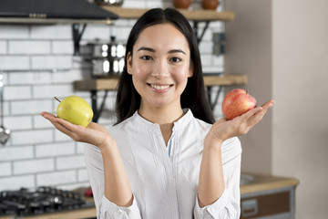 Portrait of a woman showing healthy green and red apple in kitchen