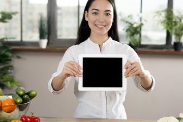 Portrait of asian woman showing blank screen digital tablet in kitchen