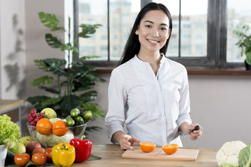 Portrait of young woman standing near kitchen counter with different types of vegetables and fruits