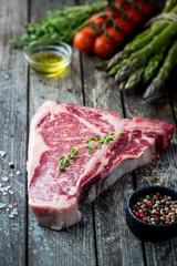 Raw T-bone Steak with fresh herbs and oil on dark wooden background