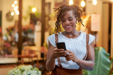 Attractive young Black woman smiling when reading text message on her smartphone