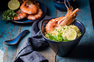 A bowl of instant Chinese noodles with green onions, red hot chilli peppers, and shrimps on a dark rustic background
