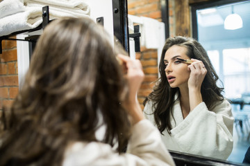 Young woman dyes her eyelashes with mascara brush. Young beautiful woman applying mascara makeup on eyes at bathroom.