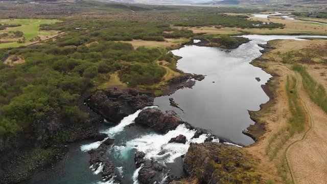 The less crowded but beautiful waterfall Glanni seen from above, surrounded by a magical Icelandic landscape with lush green bushes and majestic mountains in the background