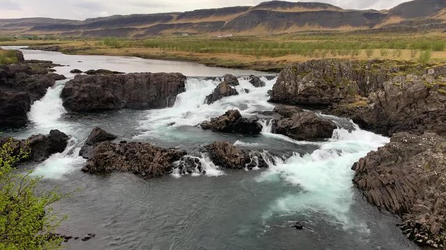 The less crowded but beautiful waterfall Glanni surrounded by a magical Icelandic landscape with lush green bushes and majestic mountains in the background