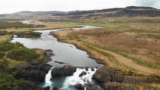 The less crowded but beautiful waterfall Glanni seen from above, surrounded by a magical Icelandic landscape with lush green bushes and majestic mountains in the background