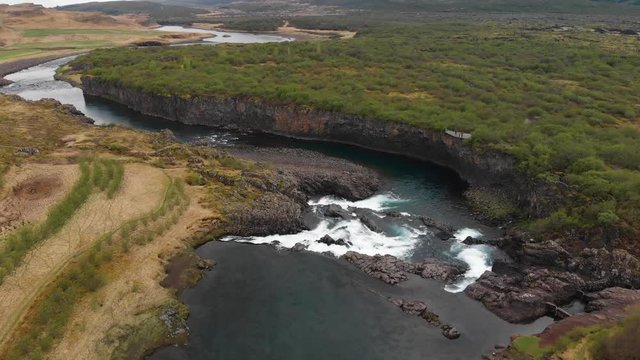 The less crowded but beautiful waterfall Glanni seen from above, surrounded by a magical Icelandic landscape with lush green bushes and majestic mountains in the background