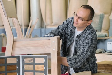 Male carpenter working in furniture joinery, master making wooden chair in wood workshop