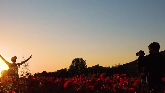 Sagoma di un fotografo e modello mentre sono in posa per uno scatto in mezzo al campo di papaveri rossi al tramonto.