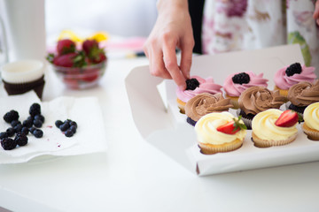 Close up of female hand topping a cupcake. Pastry chef woman making sweet dessert cake. Horizontal image