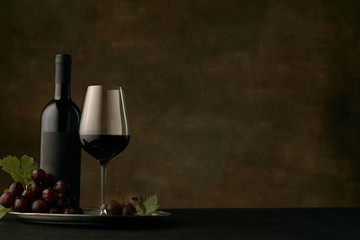 Front view of tasty fruit plate of grapes with the wine bottle and glass on dark studio background, copy space to insert your text or image. Gourmet food and drink.
