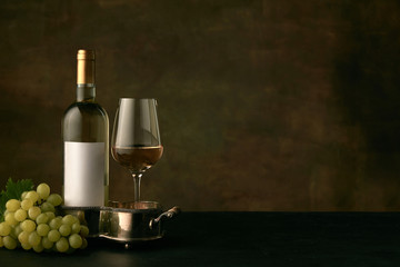 Obraz premium Front view of tasty fruit plate of grapes with the wine bottle and glass on dark studio background, copy space to insert your text or image. Gourmet food and drink.