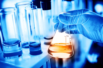 Flask in scientist hand with lab glassware background in laboratory. Science or chemical research and development concept. 