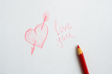 Heart drawn on paper, the inscription love you and a red pencil on white paper.